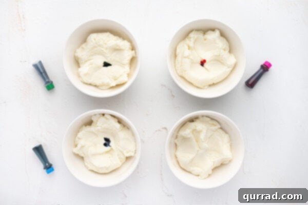 Four separate bowls containing portions of the cream cheese mint mixture, with small dots of food coloring added to each, ready for mixing.