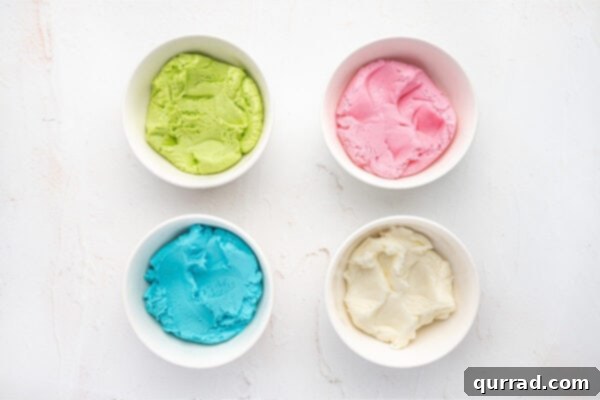 Four separate bowls displaying dyed cream cheese mint dough in vibrant green, pink, blue, and white, after the coloring has been mixed in.