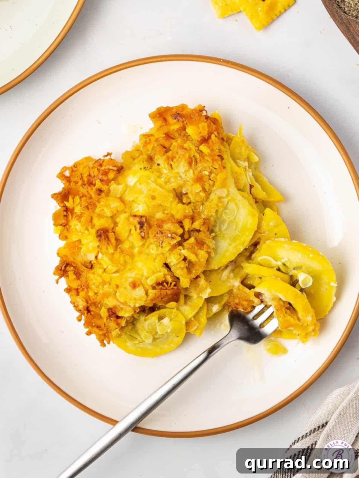 Golden Squash Bake 4 A serving of yellow squash casserole on a white plate, showcasing its golden crust and tender interior, with a fork ready to dig in.