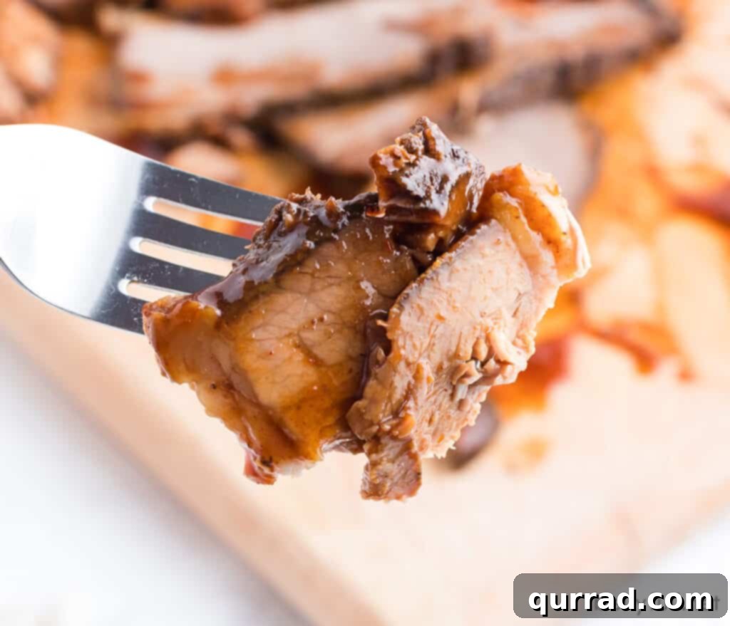 Close-up of a perfectly cooked piece of barbecue beef brisket held on a fork, highlighting its tender, juicy texture and flavorful crust.