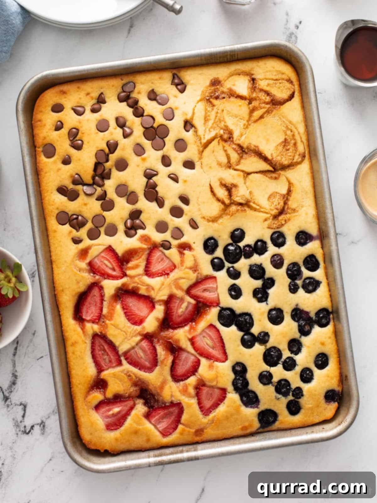 Sheet pan pancakes divided into four sections with berries, chocolate chips, and cinnamon swirl, ready to serve for a family breakfast.