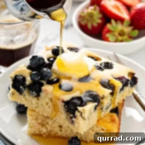 Two square blueberry pancakes stacked with maple syrup being poured on top, highlighting the perfect texture of sheet pan pancakes.