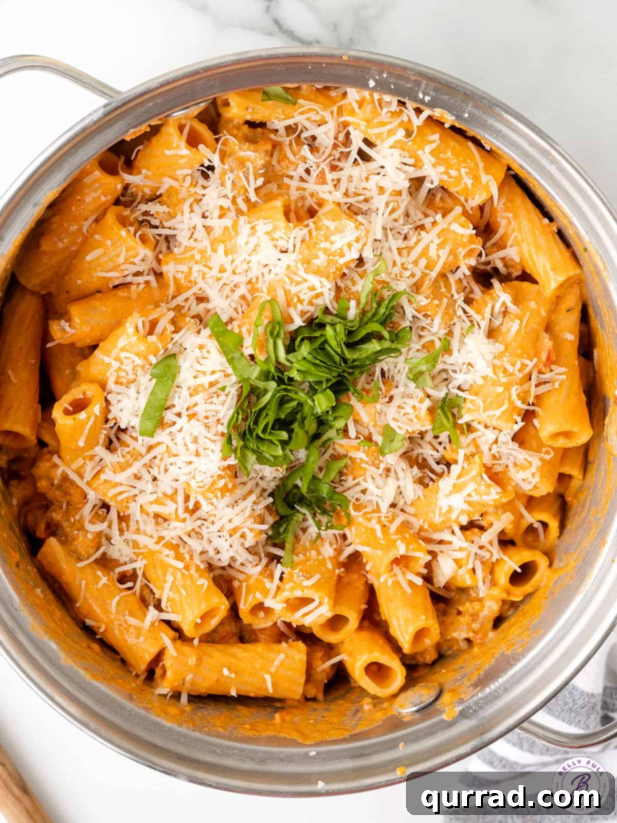 Effortless One-Pan Sausage Pasta 3 Overhead view of creamy rigatoni pasta in a large pot, garnished with parmesan and basil