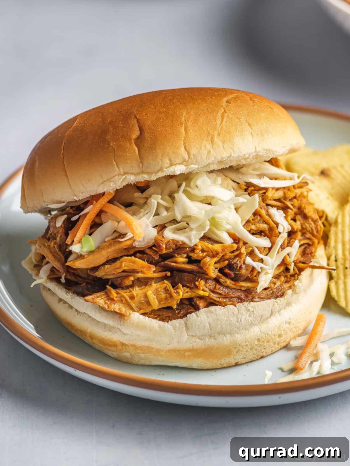 Set-and-Forget BBQ Chicken 2 A close-up of a delectable pulled BBQ chicken sandwich, generously filled with shredded chicken and topped with creamy coleslaw.