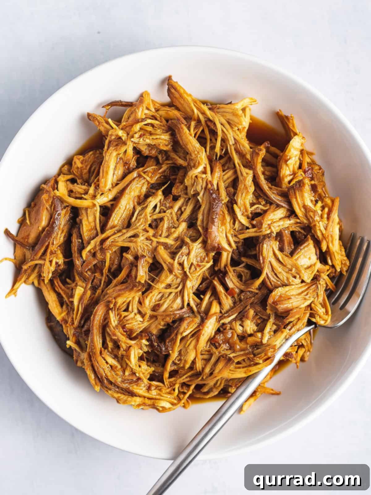 Set-and-Forget BBQ Chicken 3 A white bowl brimming with perfectly slow-cooked shredded BBQ chicken, glistening with rich, sweet, and tangy sauce.