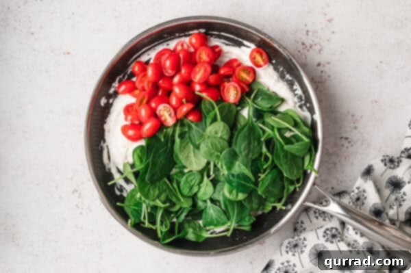 Fresh baby spinach and halved cherry tomatoes added to the cream sauce in a pan