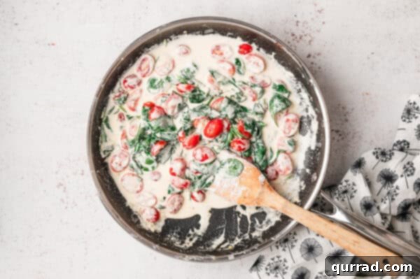 Wilted spinach and softened cherry tomatoes mixed into the creamy sauce in a pan