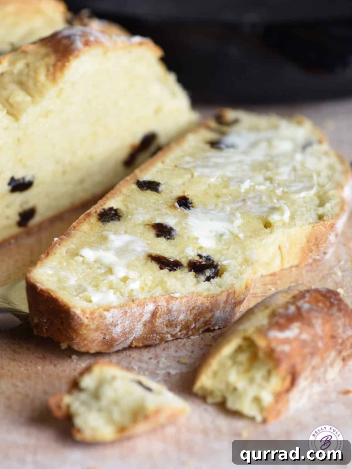 A slice of freshly baked Irish Soda Bread, spread generously with butter, showcasing its delightful texture and raisins.