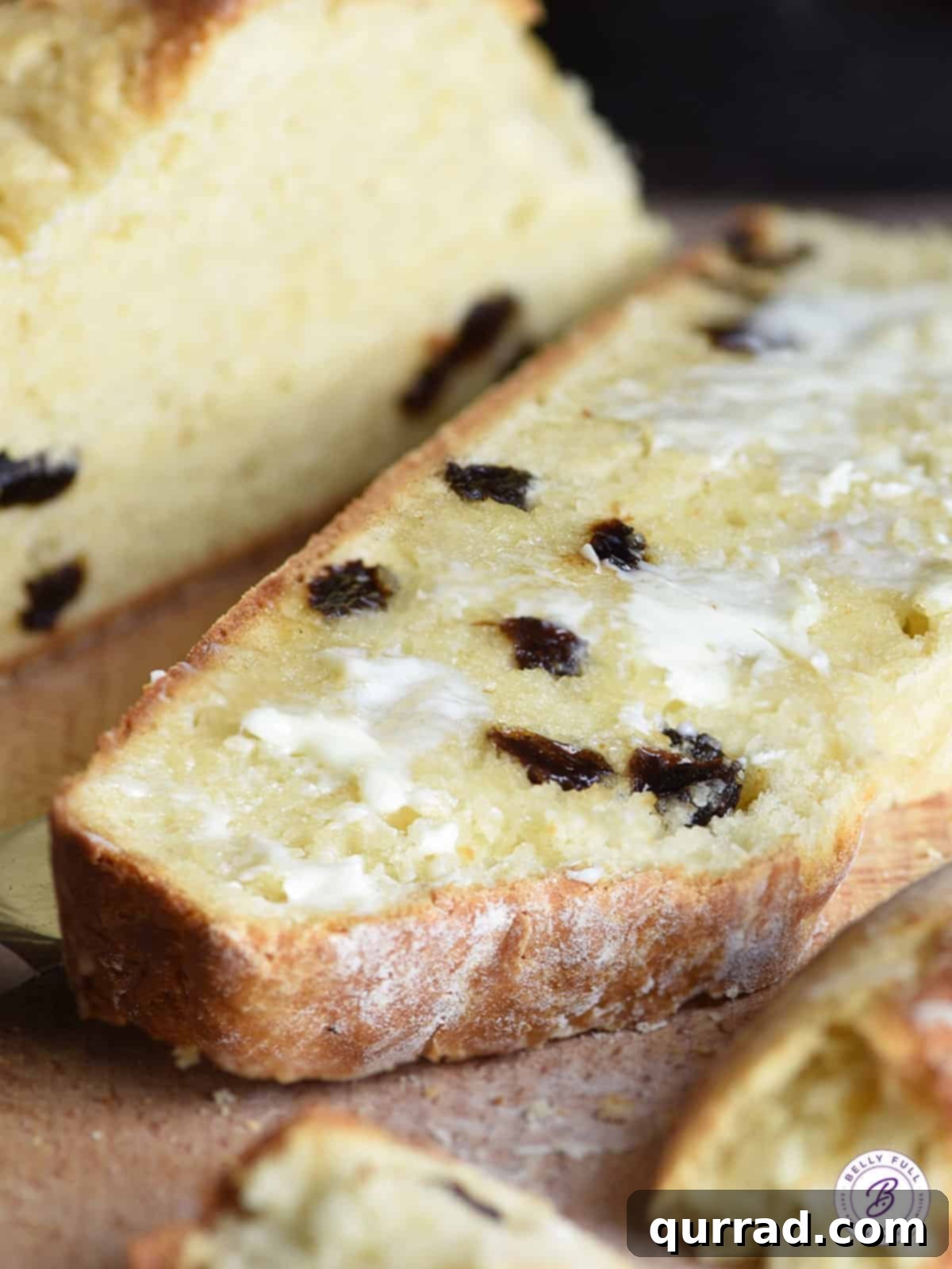 A close-up shot of a slice of buttered Irish Soda Bread with visible raisins and a rustic crust.