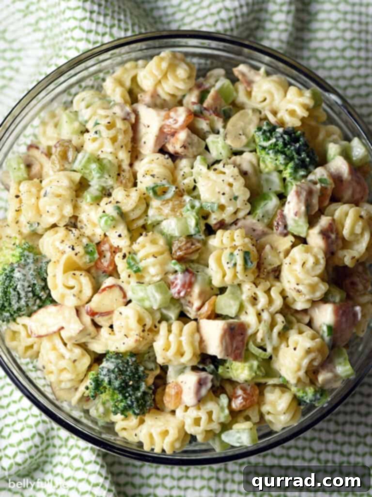 Hearty Chicken and Broccoli Pasta Salad 2 A vibrant top-down view of Chicken Broccoli Pasta Salad in a large serving bowl, garnished with fresh parsley. It features tender chicken, bright green broccoli, golden raisins, and celery, all coated in a creamy dressing.