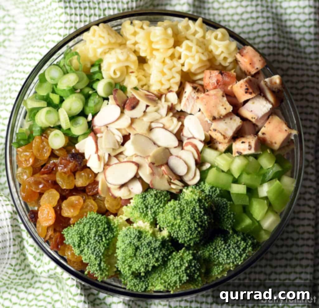 Hearty Chicken and Broccoli Pasta Salad 4 Individual ingredients for Chicken Broccoli Pasta Salad laid out in glass bowls: pasta, diced chicken, broccoli florets, golden raisins, celery, sliced almonds, and scallions, with dressing ingredients in the foreground.
