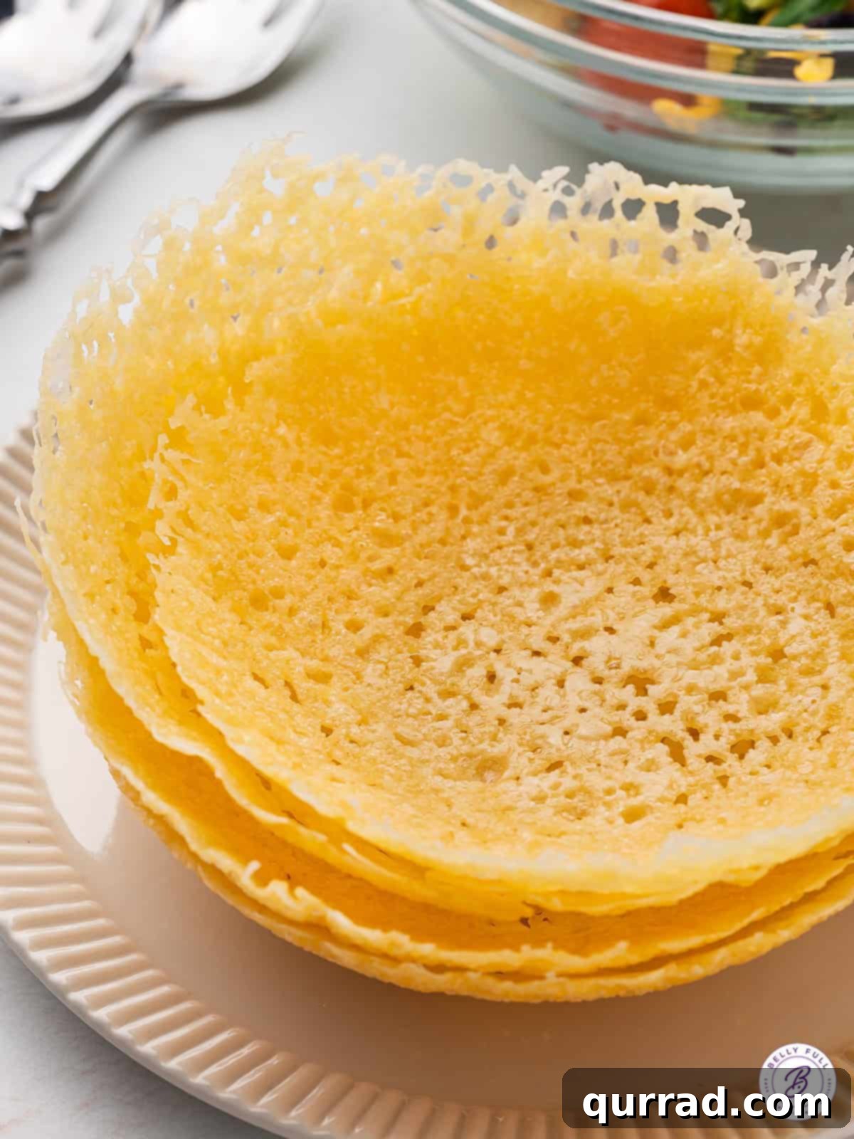 Edible Parmesan Bowls 2 Four golden, crispy edible cheese bowls stacked neatly, showcasing their perfect shape and readiness for use. Each bowl boasts a rich, golden-brown hue and a distinctive texture, inviting delicious fillings.