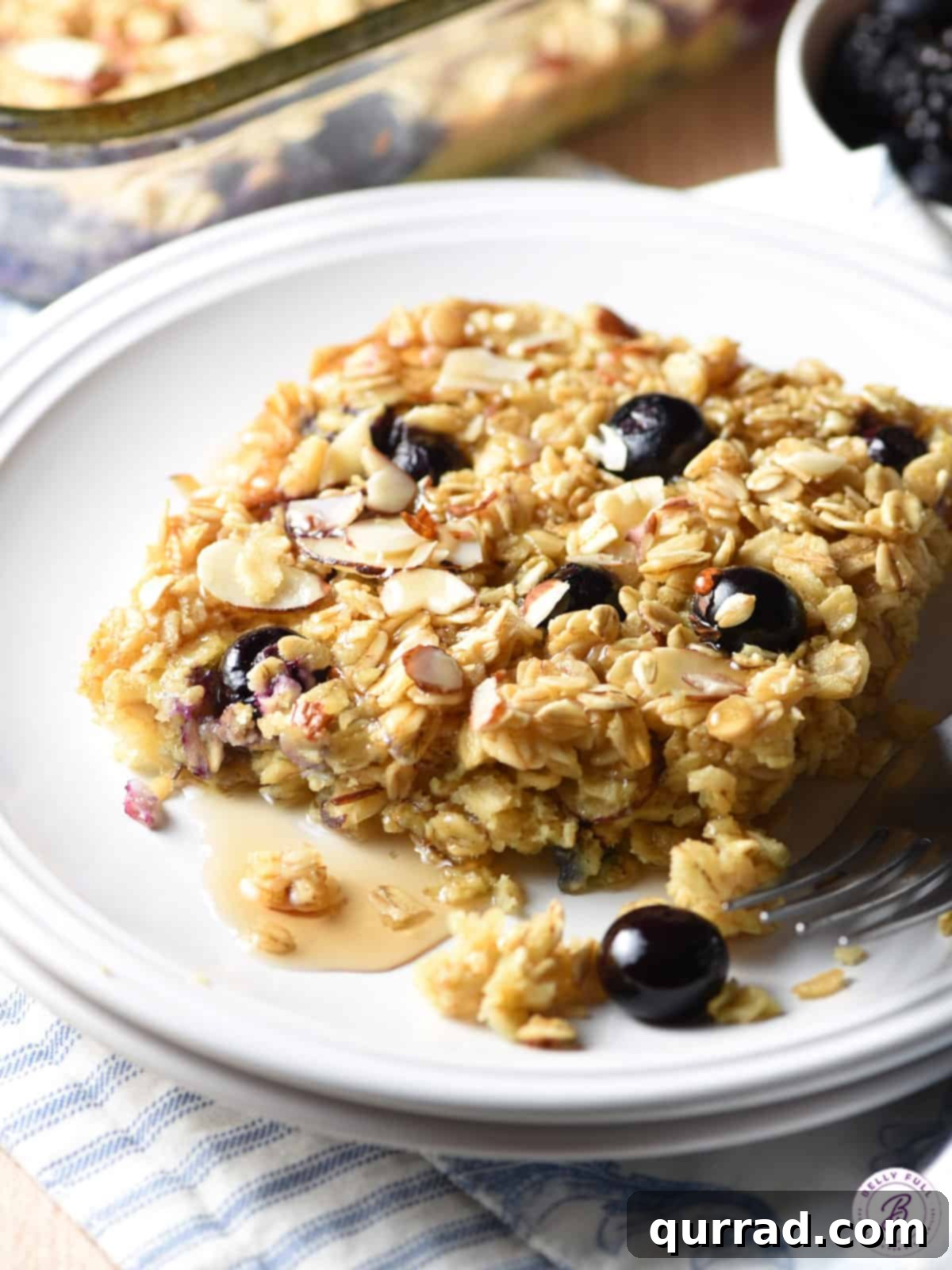 Cozy Blueberry Baked Oats 2 Baked oatmeal square on a plate with blueberries and maple syrup.