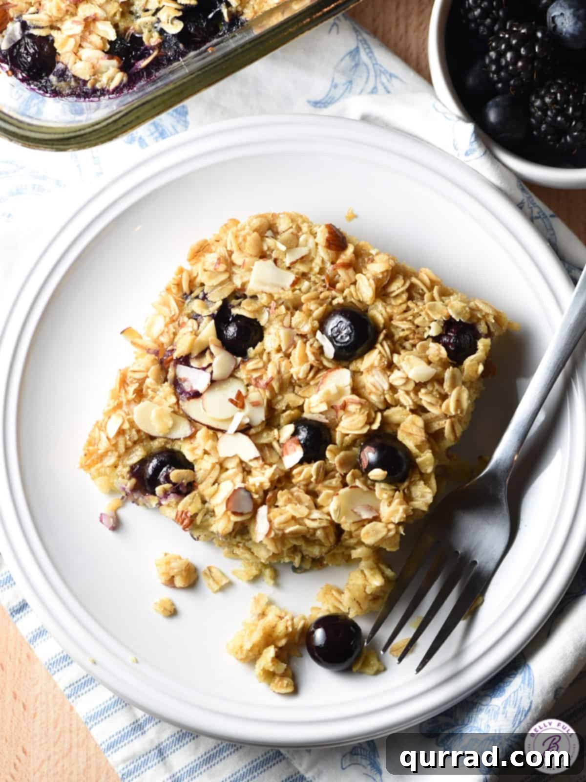 Cozy Blueberry Baked Oats 8 Slice of baked oatmeal with blueberries and almonds on a plate with a fork.