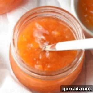 Close-up of vibrant peach jam in a small glass jar, perfect for spreading.