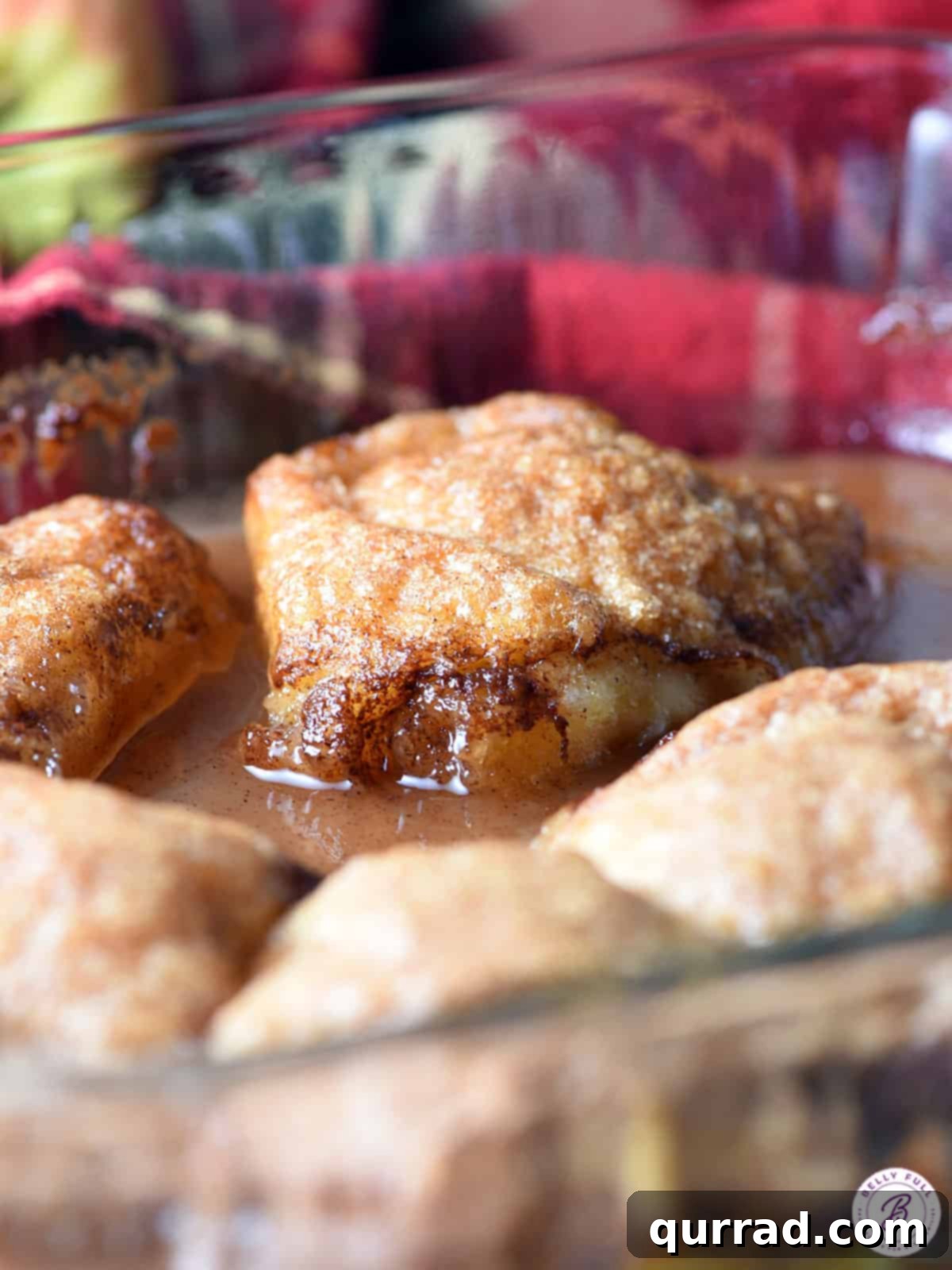 Effortless Baked Apple Bliss 7 Freshly baked crescent roll apple dumplings in a glass baking dish, glistening with sauce.