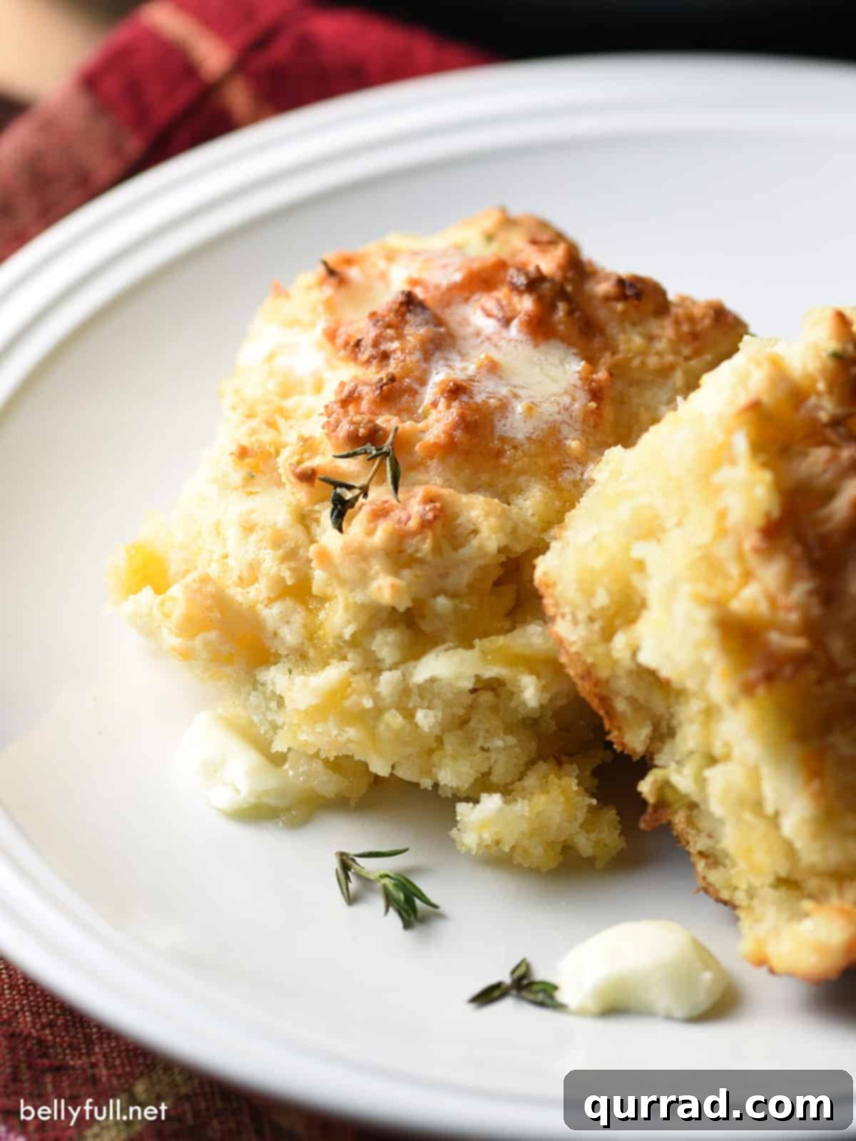 Sweet & Savory Apple-Cheddar Skillet Biscuits 2 Two golden-brown apple cheddar drop biscuits on a white plate with melted butter drizzled over them.