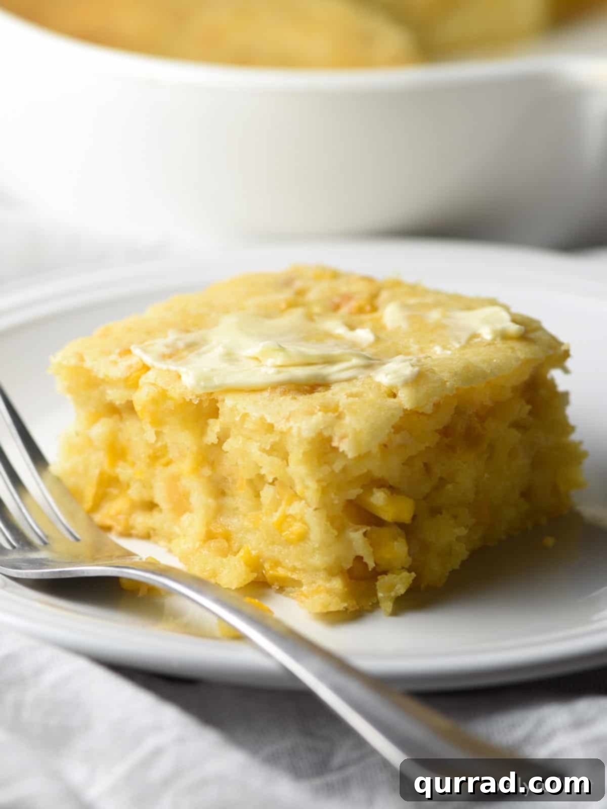 Piece of cornbread casserole on a white plate with a fork, ready to be enjoyed.