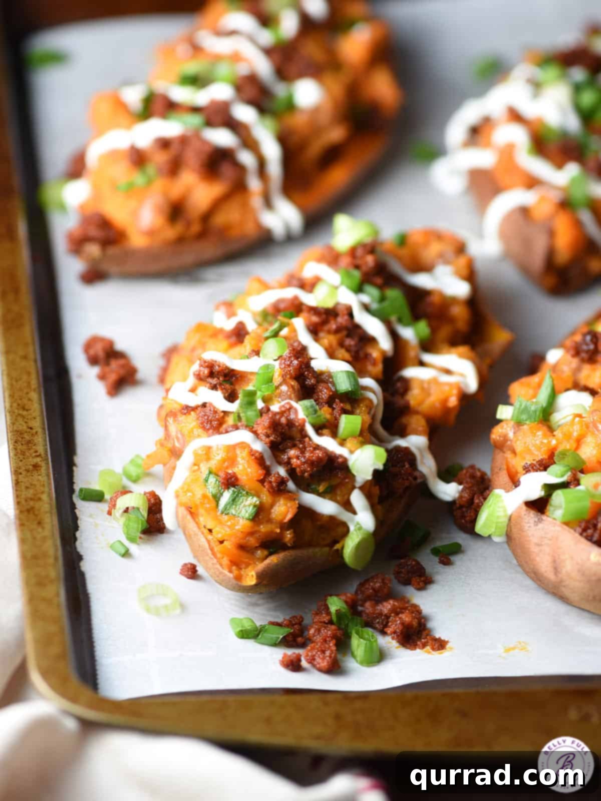 Close-up of a twice baked sweet potato with chorizo and sour cream drizzle, garnished with fresh scallions