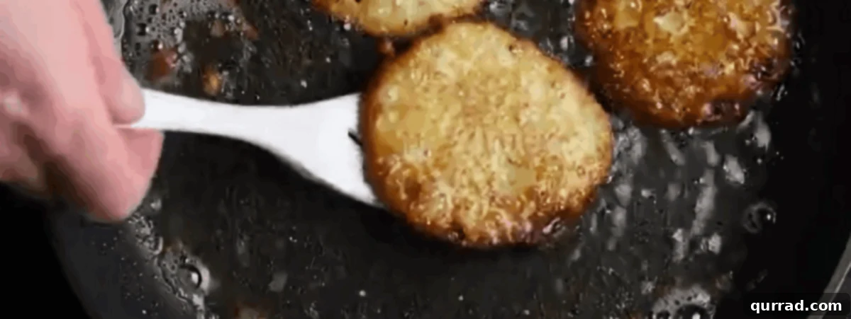 Crispy Potato Pancakes 6 Potato latkes frying in a pan, achieving a golden-brown color.