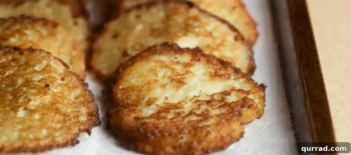 Crispy Potato Pancakes 7 Fried potato latkes neatly arranged on a paper towel-lined baking sheet for draining.