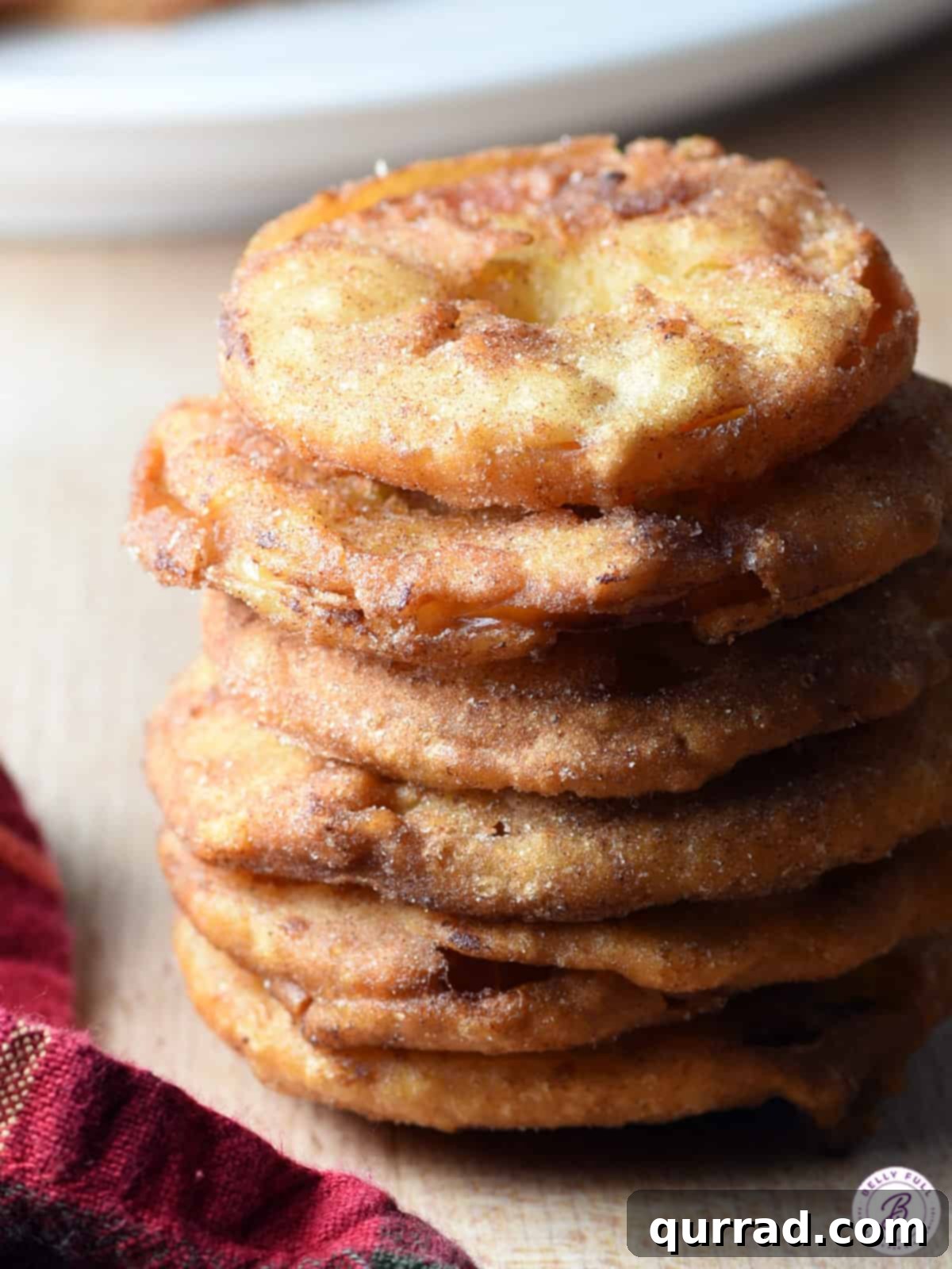 Tall stack of golden-brown Apple Fritter Rings dusted with cinnamon sugar, invitingly arranged