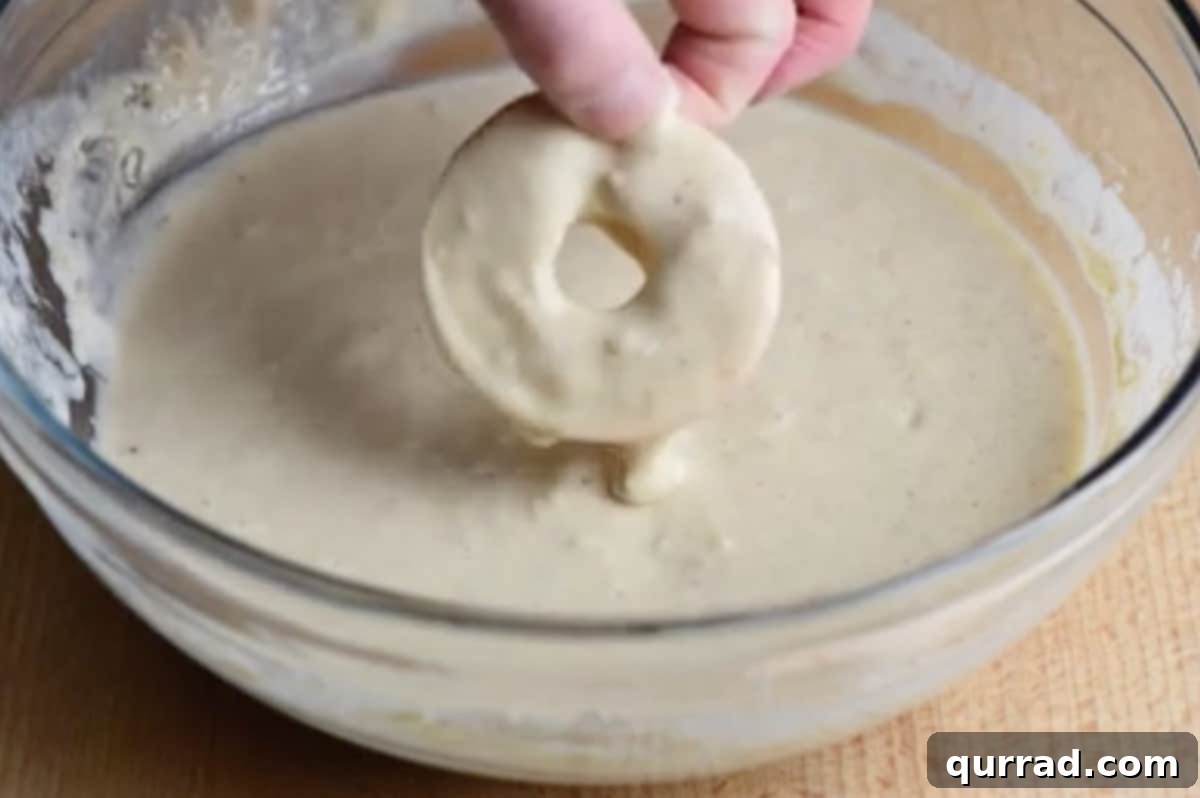 A sliced apple ring being submerged and coated in the thick batter.