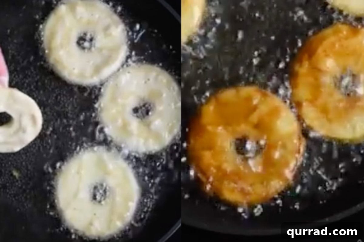 Several battered apple rings sizzling and turning golden brown in hot oil in a deep pan.