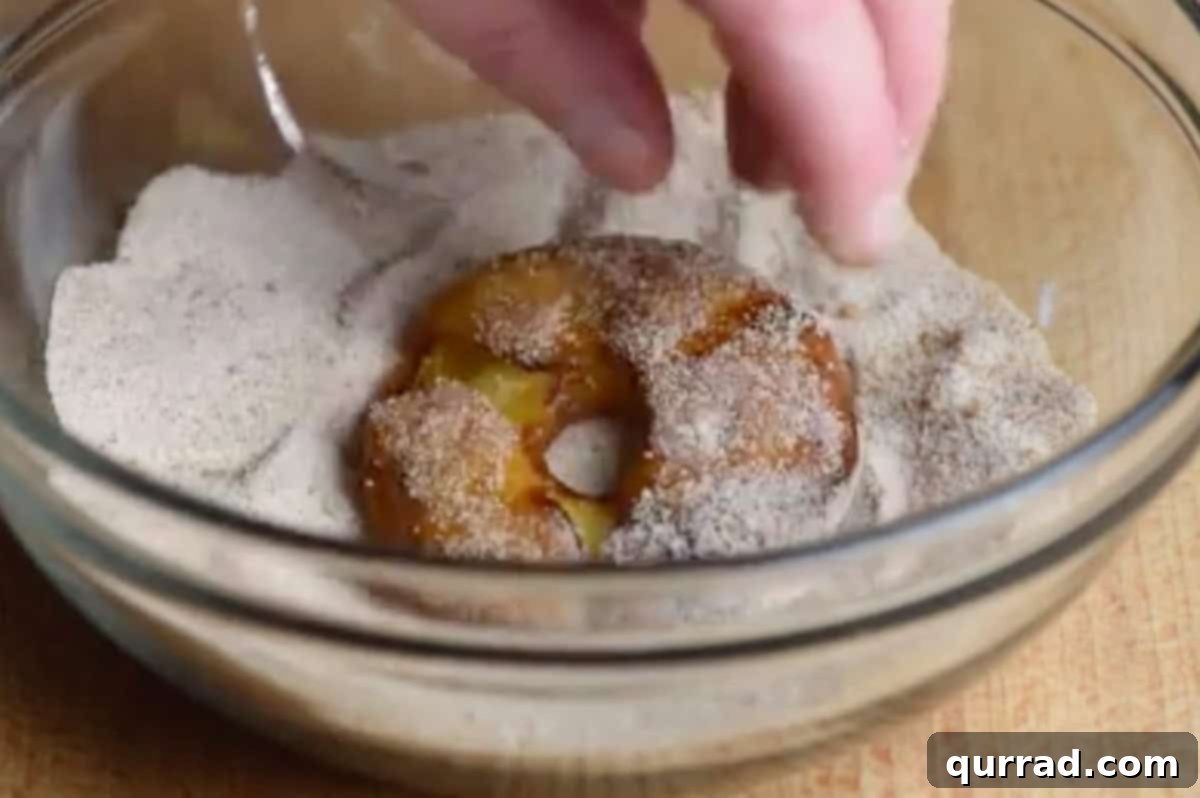 A fried apple ring being tossed in a bowl of cinnamon-sugar mixture for coating.