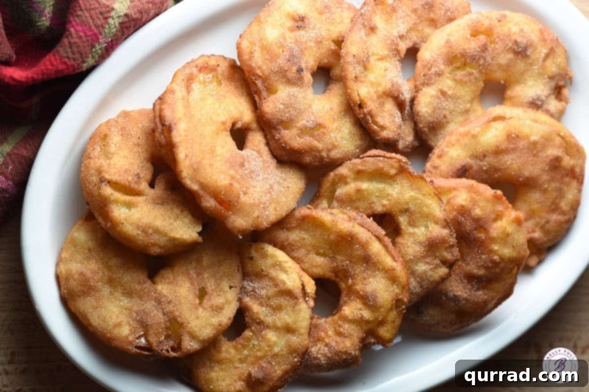 Several overlapping fried apple rings artfully arranged on a serving platter, glistening with cinnamon sugar.