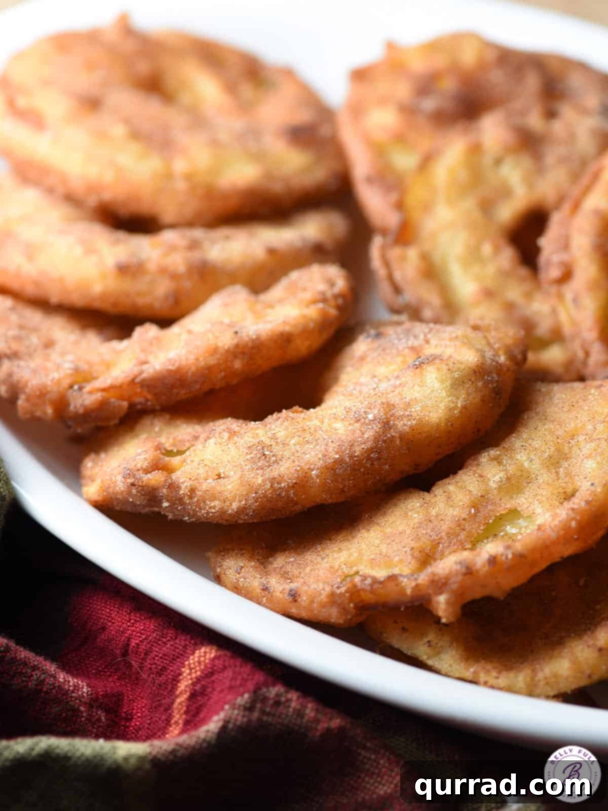 Several overlapping fried apple rings laying flat on a white plate, showcasing their perfect golden color and cinnamon-sugar coating.