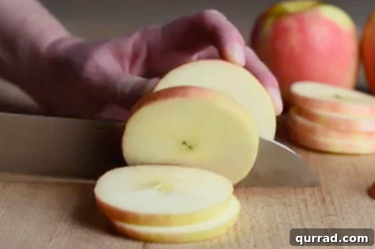 A vibrant red apple being carefully sliced into rounds on a cutting board.