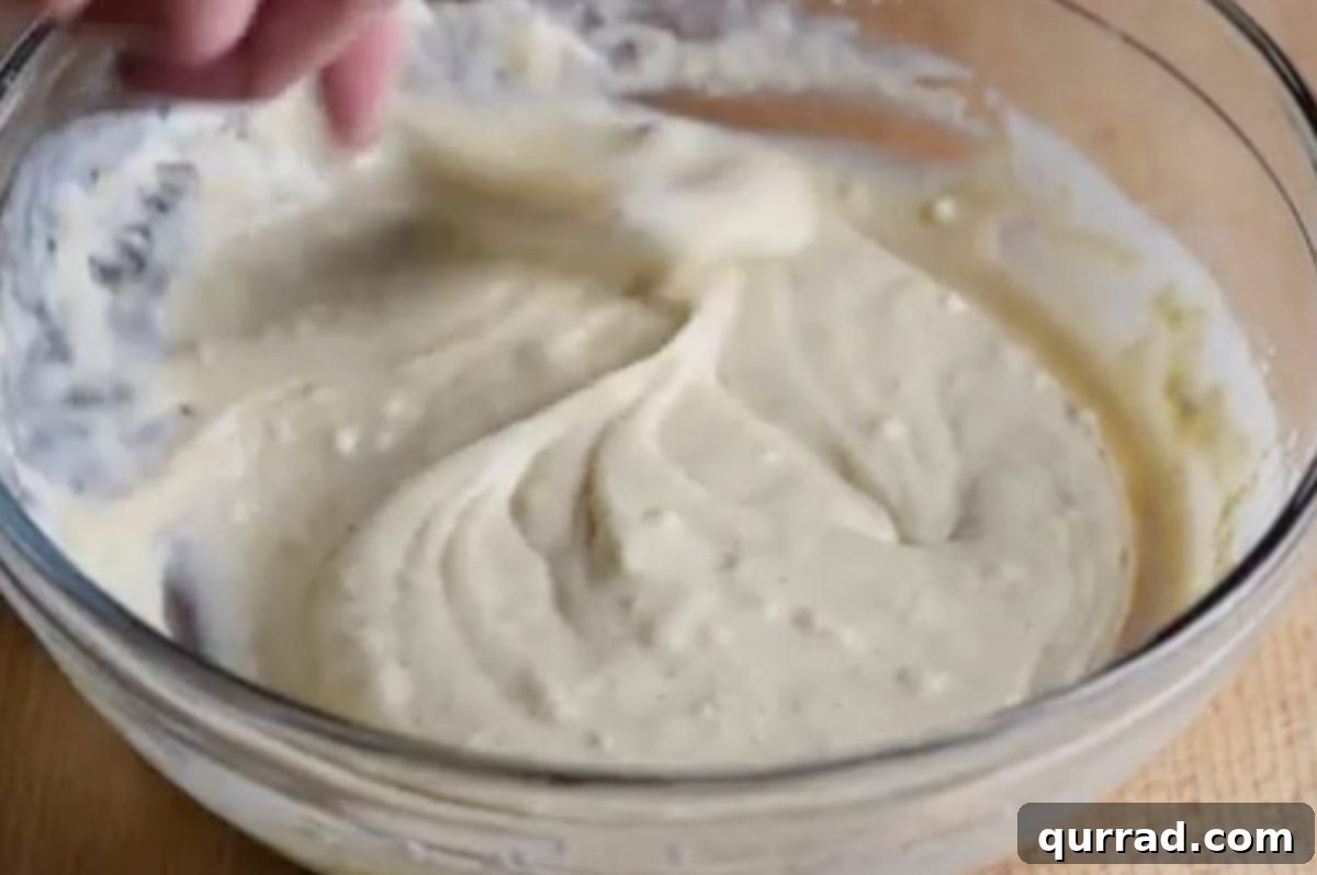 A thick, spiced batter for apple fritters resting in a mixing bowl, ready for dipping.