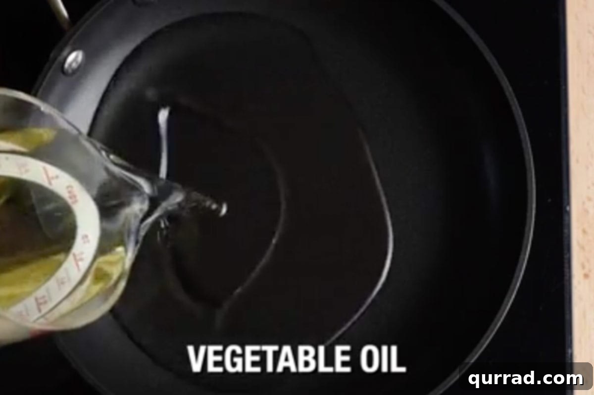 Clear vegetable oil being poured into a large, deep heavy-bottomed pan, preparing for frying.