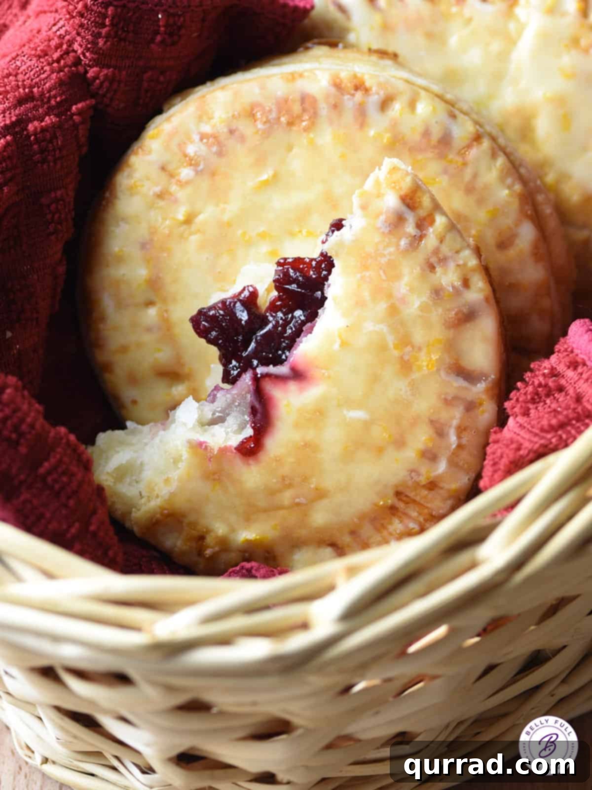 A perfectly baked cranberry hand pie, broken in half to reveal its luscious, ruby-red filling, resting on a rustic wooden surface. The flaky golden crust is visible, inviting a delightful bite.