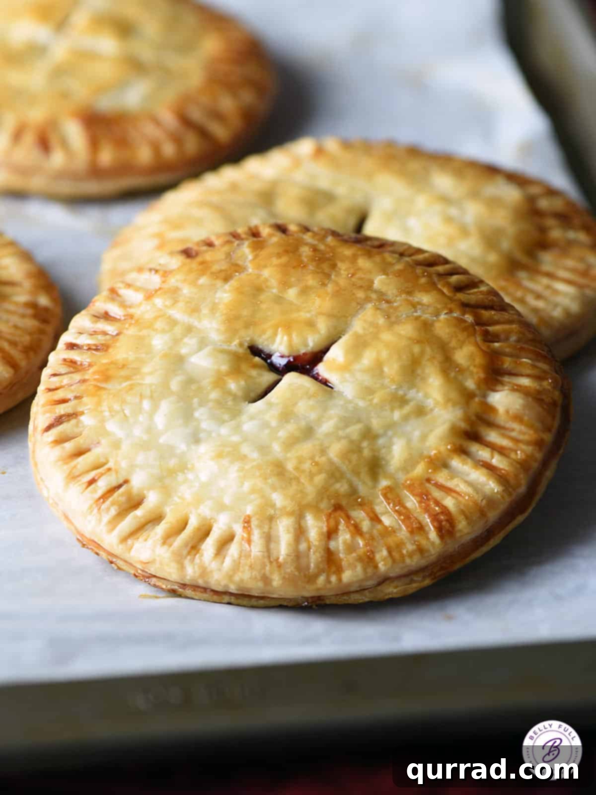 A batch of golden-brown baked cranberry hand pies cooling on parchment paper on a baking sheet, showcasing their perfectly crimped edges and glistening crusts.
