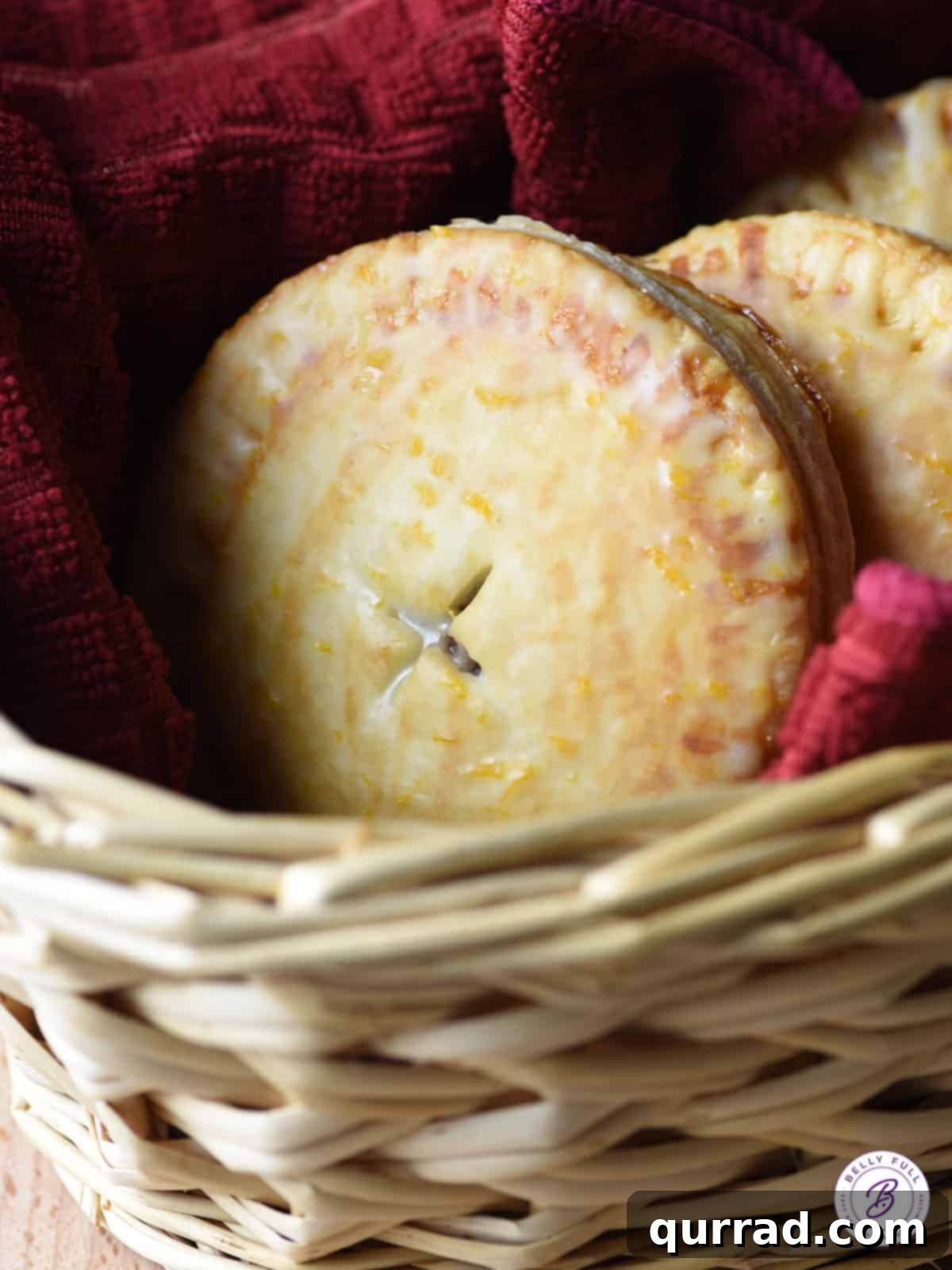 A charming collection of glazed cranberry hand pies nestled in a rustic wicker basket, ready for serving. Their glossy, bright tops contrast beautifully with the golden crusts.