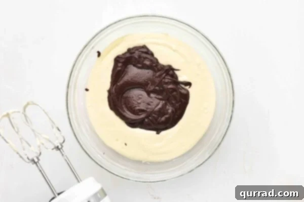 melted chocolate on top of whipped sweetened cream cheese in glass mixing bowl
