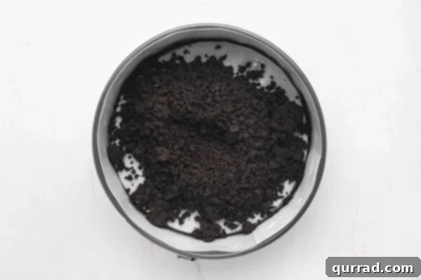 oreo cookie crumbs being pressed into the bottom of a springform pan