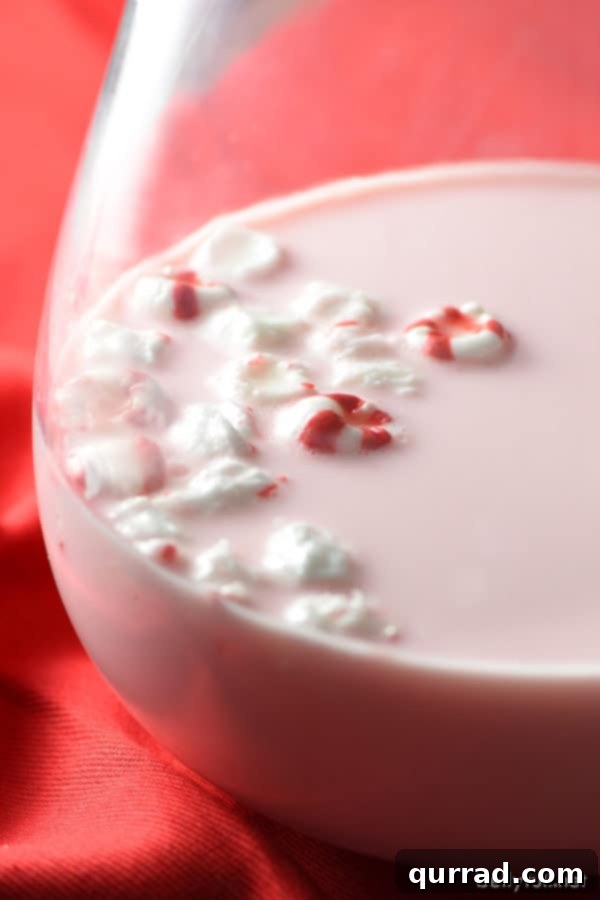 Glass pitcher filled with pink peppermint milk, surrounded by loose peppermint candies