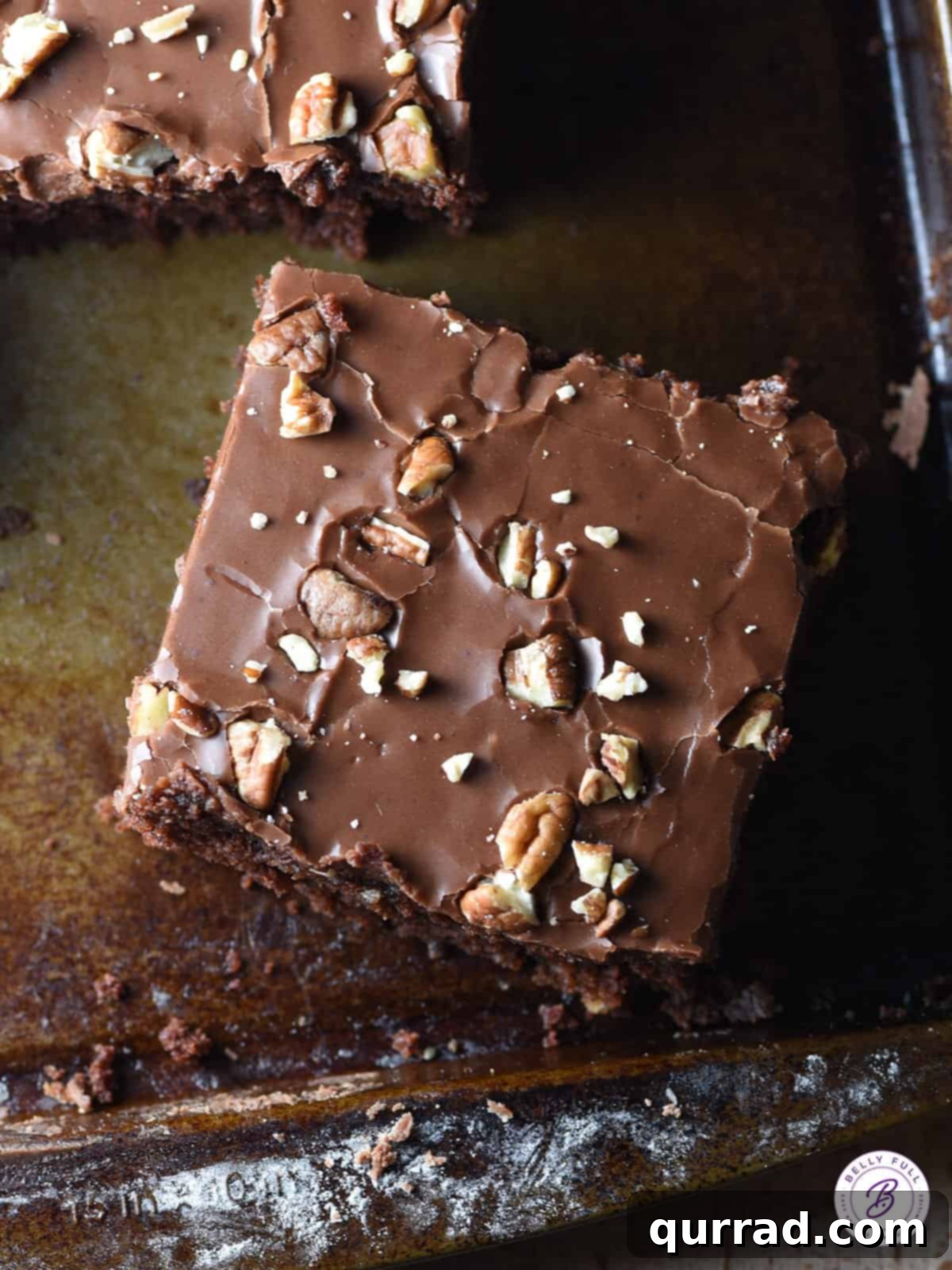 The ultimate Texas Sheet Cake: A rich, fudgy, moist chocolate cake made with buttermilk, coated in warm chocolate icing and sprinkled with toasted pecans. Heaven on a plate, ready to be enjoyed! An overhead shot of a freshly baked and frosted Texas Sheet Cake, generously sprinkled with toasted pecans, sliced into neat squares on a sheet pan, ready for serving.