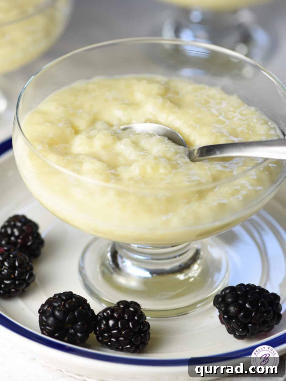 A close-up of a glass cup filled with creamy homemade tapioca pudding, topped with a spoon, highlighting its inviting texture.