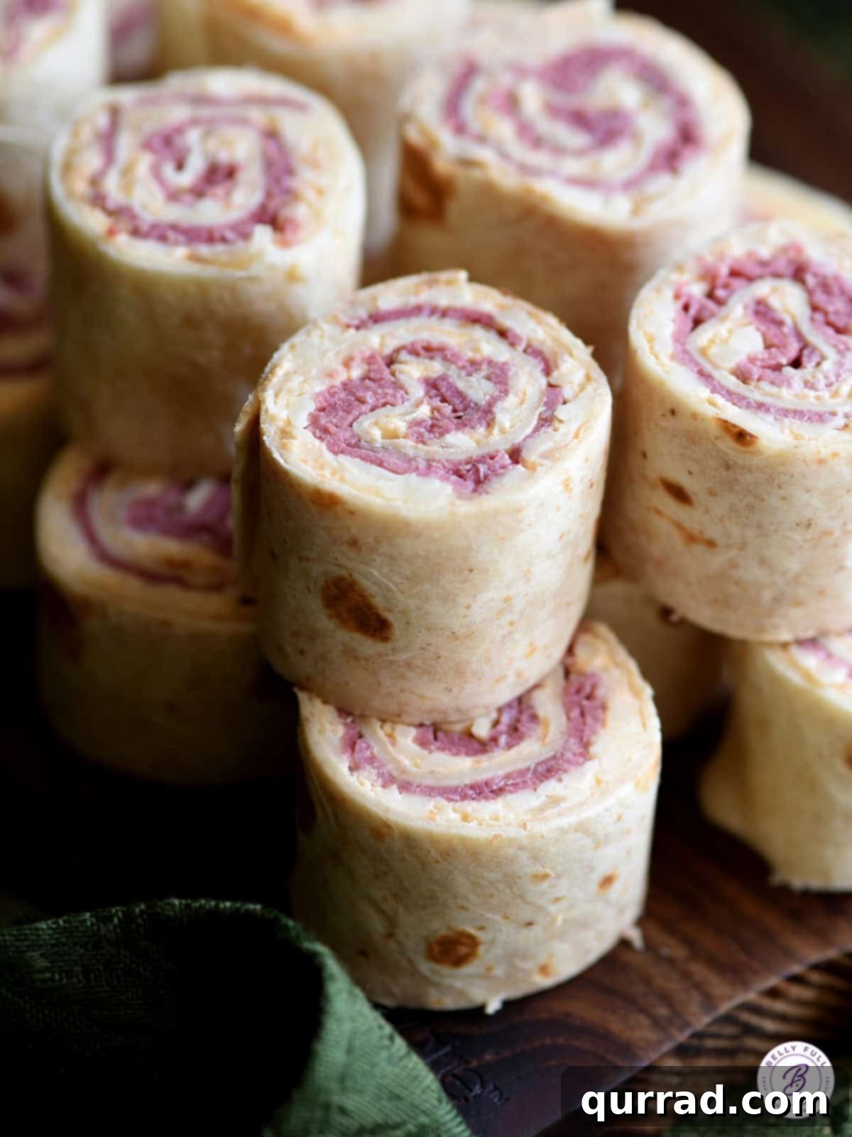 Reuben Swirls 4 Stacked Reuben Pinwheels appetizer on a rustic serving board, featuring the distinct layers of corned beef, Swiss cheese, sauerkraut, and dressing within perfectly rolled tortillas, viewed from a slightly different angle.