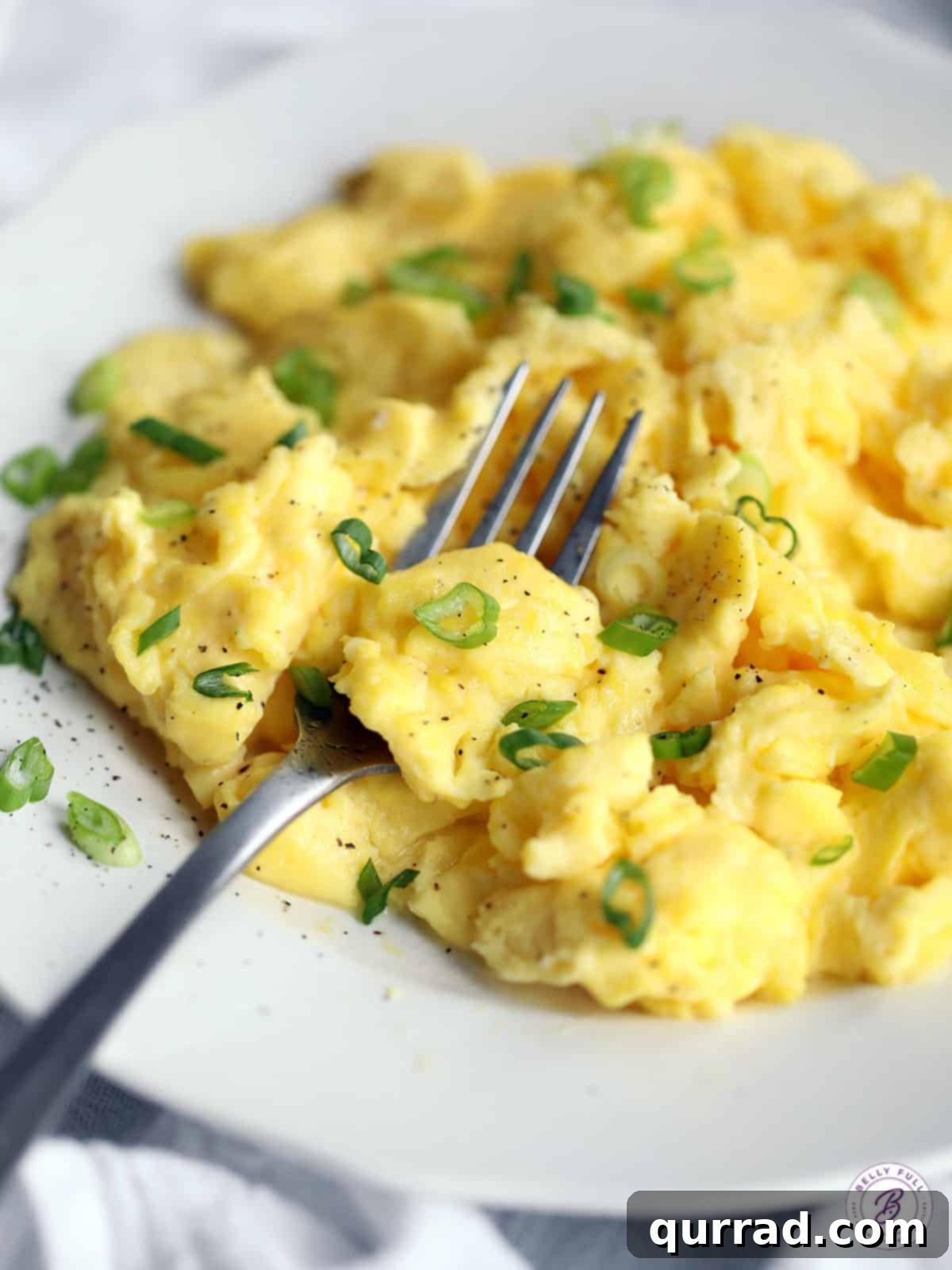 Unlock the Art of Perfect Scrambled Eggs 4 close up of fluffy scrambled eggs on fork garnished with pepper and scallions