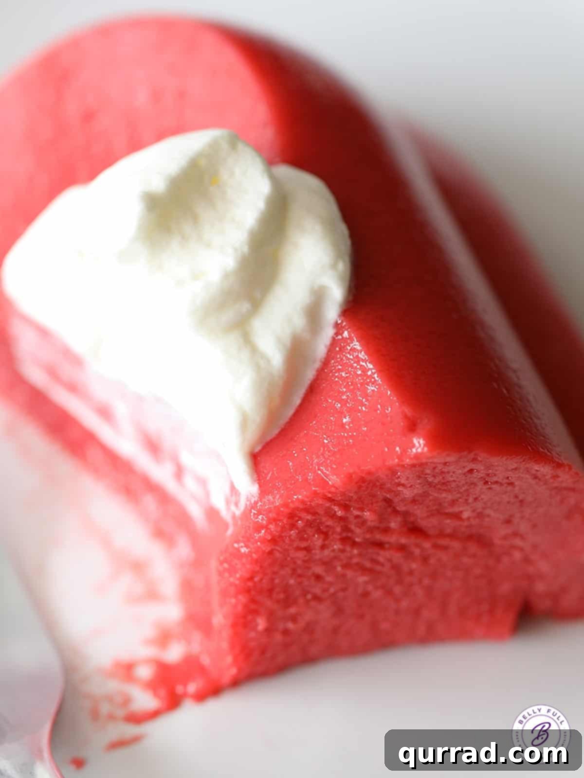 Velvety Strawberry Swirl Jello 5 A delightful close-up of a creamy strawberry jello slice adorned with fresh whipped cream, ready to be enjoyed as a refreshing dessert.