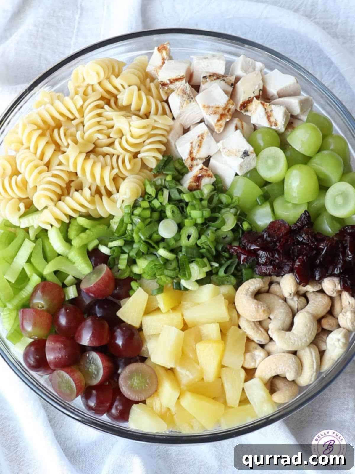 Hearty Cashew Chicken Pasta Medley 3 Separated ingredients for creamy chicken pasta salad, including pasta, chicken, pineapple, grapes, and cashews, arranged neatly in bowls.