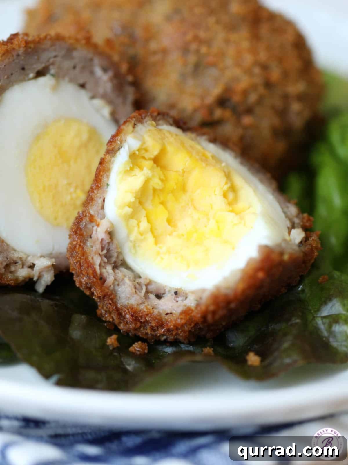 A delicious Scotch Egg, halved to show its perfectly cooked center and crunchy coating. Scotch egg sliced in half revealing a perfectly cooked yolk and crispy exterior