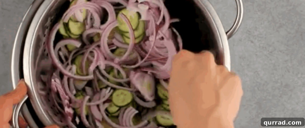 Refreshing Creamy Cucumber Medley 4 Sliced cucumbers and red onions draining in a colander over a bowl.