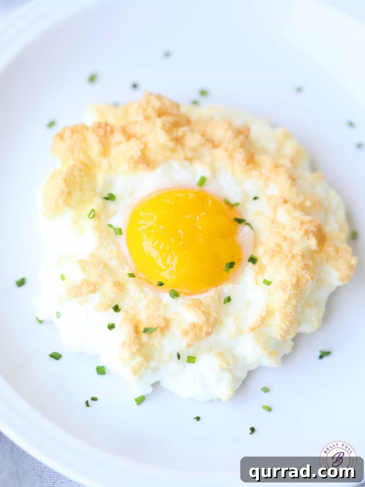 Pillowy Baked Eggs 2 overhead cloud egg garnished with fresh chives, showcasing its fluffy white exterior and vibrant yellow yolk.