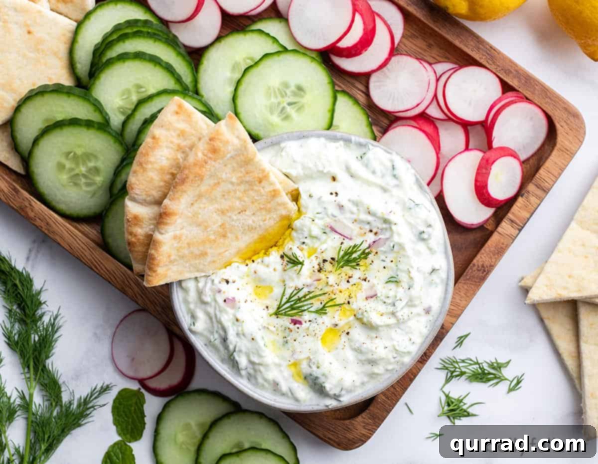 Refreshing Greek Cucumber Yogurt Dip 4 An overhead shot of a bowl of freshly made Tzatziki sauce, surrounded by colorful dippers like pita bread, cucumber slices, and radish rounds.